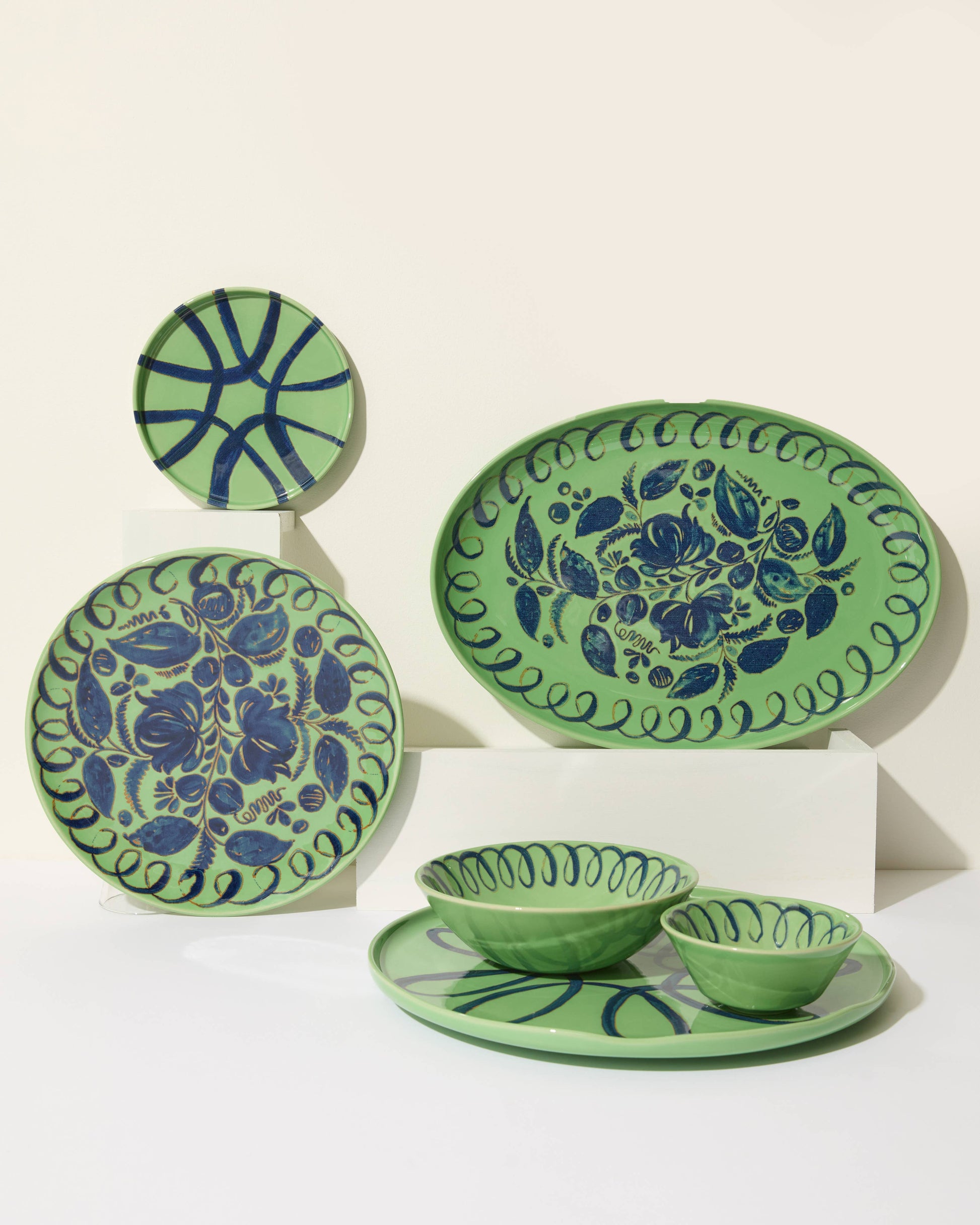 Set of green ceramic plates with blue floral patterns on a white background