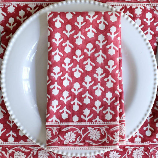 A folded red napkin with a white floral and botanical block-print pattern, placed on a white plate over a matching red and white tablecloth.
