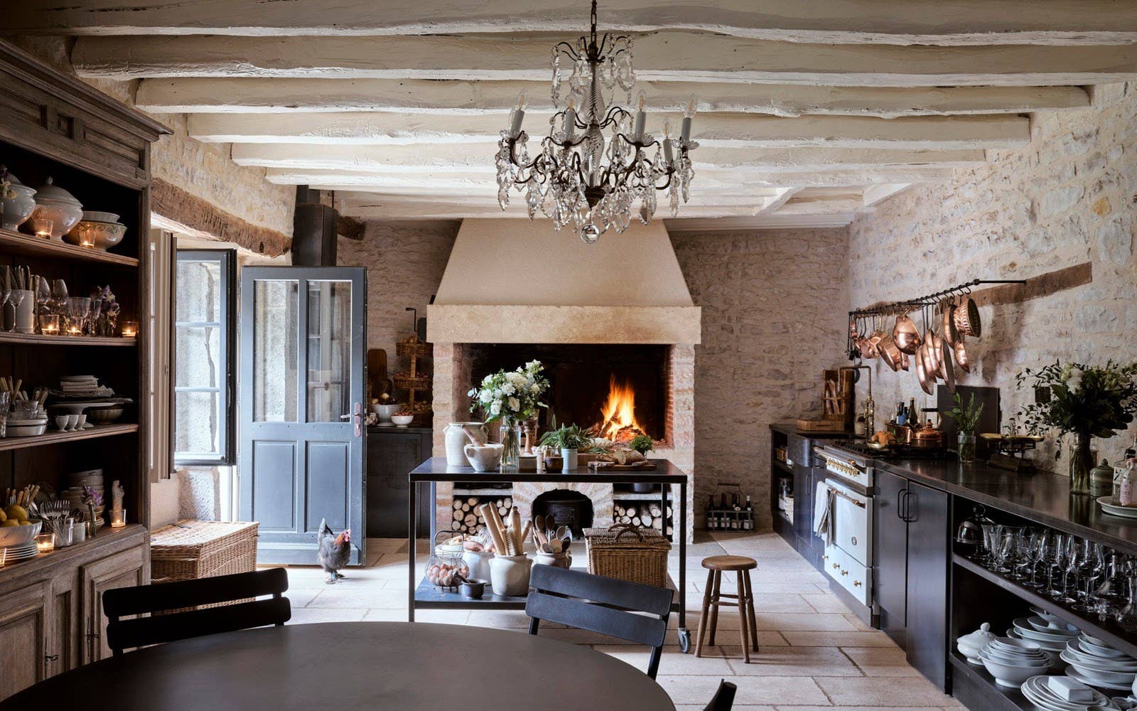Cozy kitchen with stone walls, wooden beams, and a chandelier.