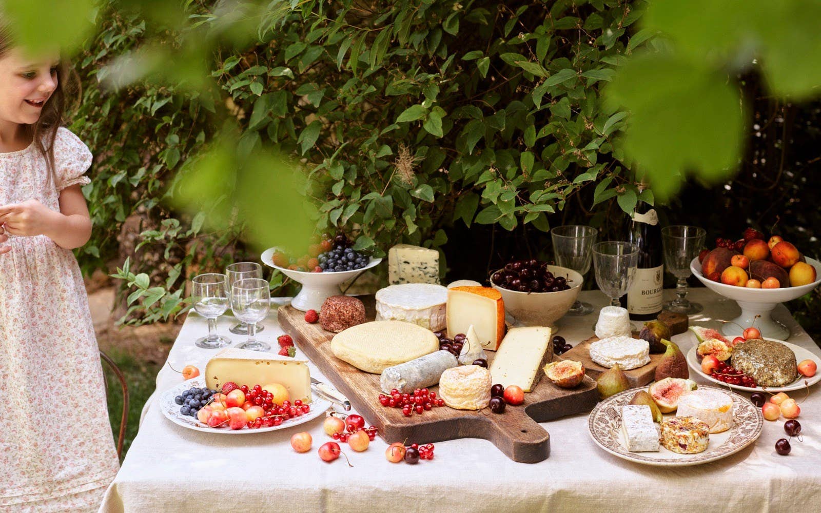 Outdoor setting with a table laden with food and a child standing nearby.
