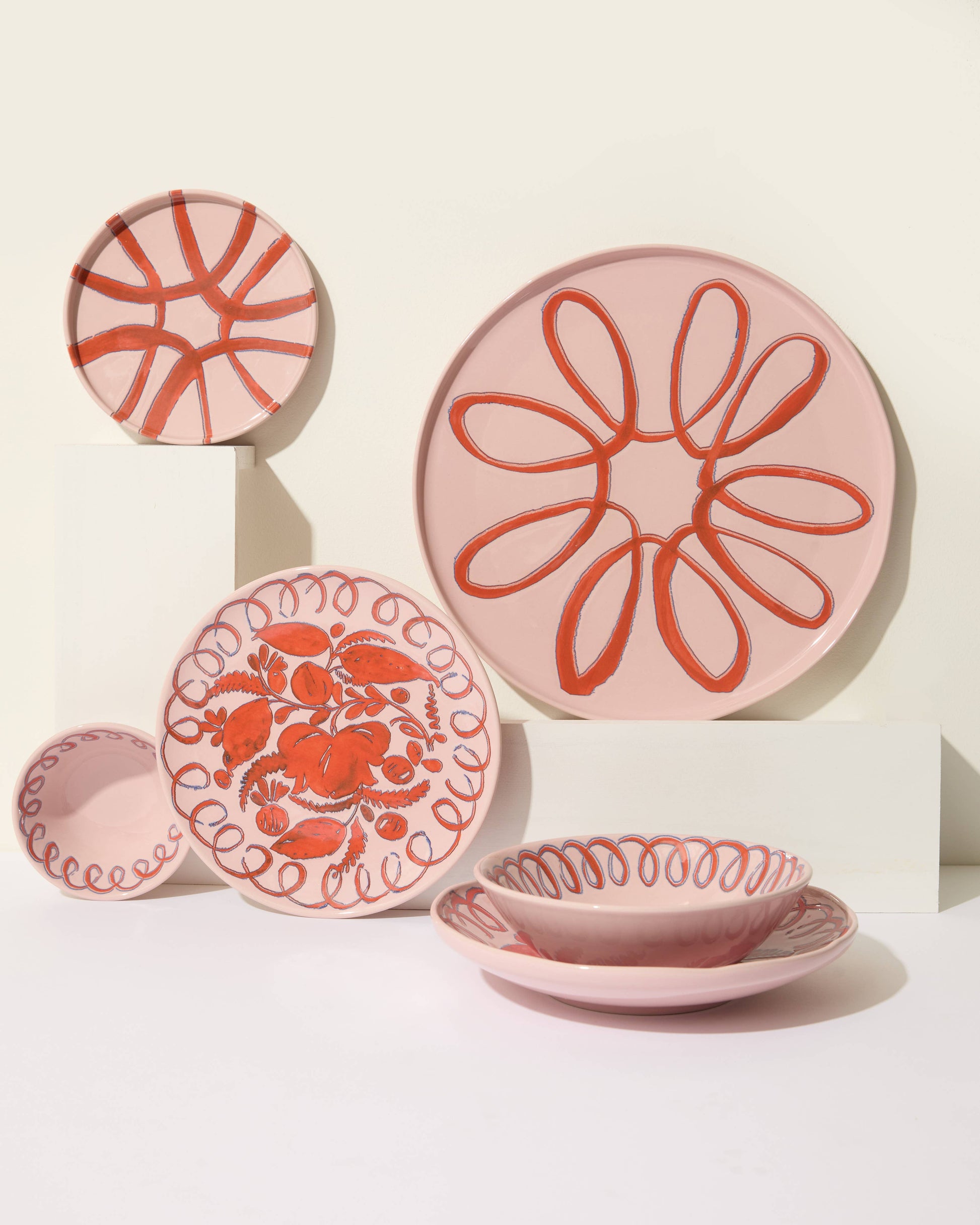 Set of pink ceramic plates with red floral patterns on a white background