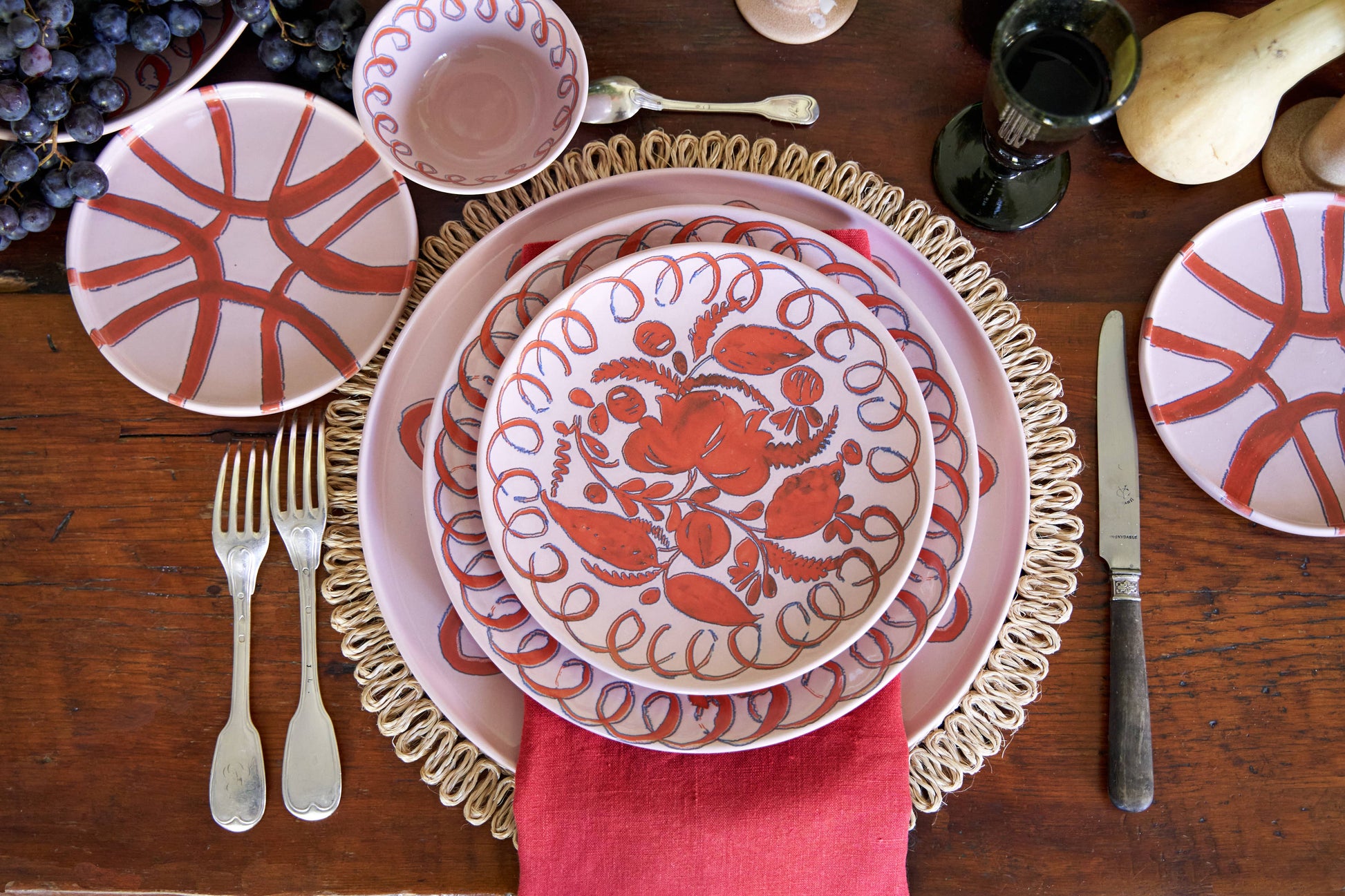 Dining table setting with red and white patterned plates, silverware, and a pink napkin.