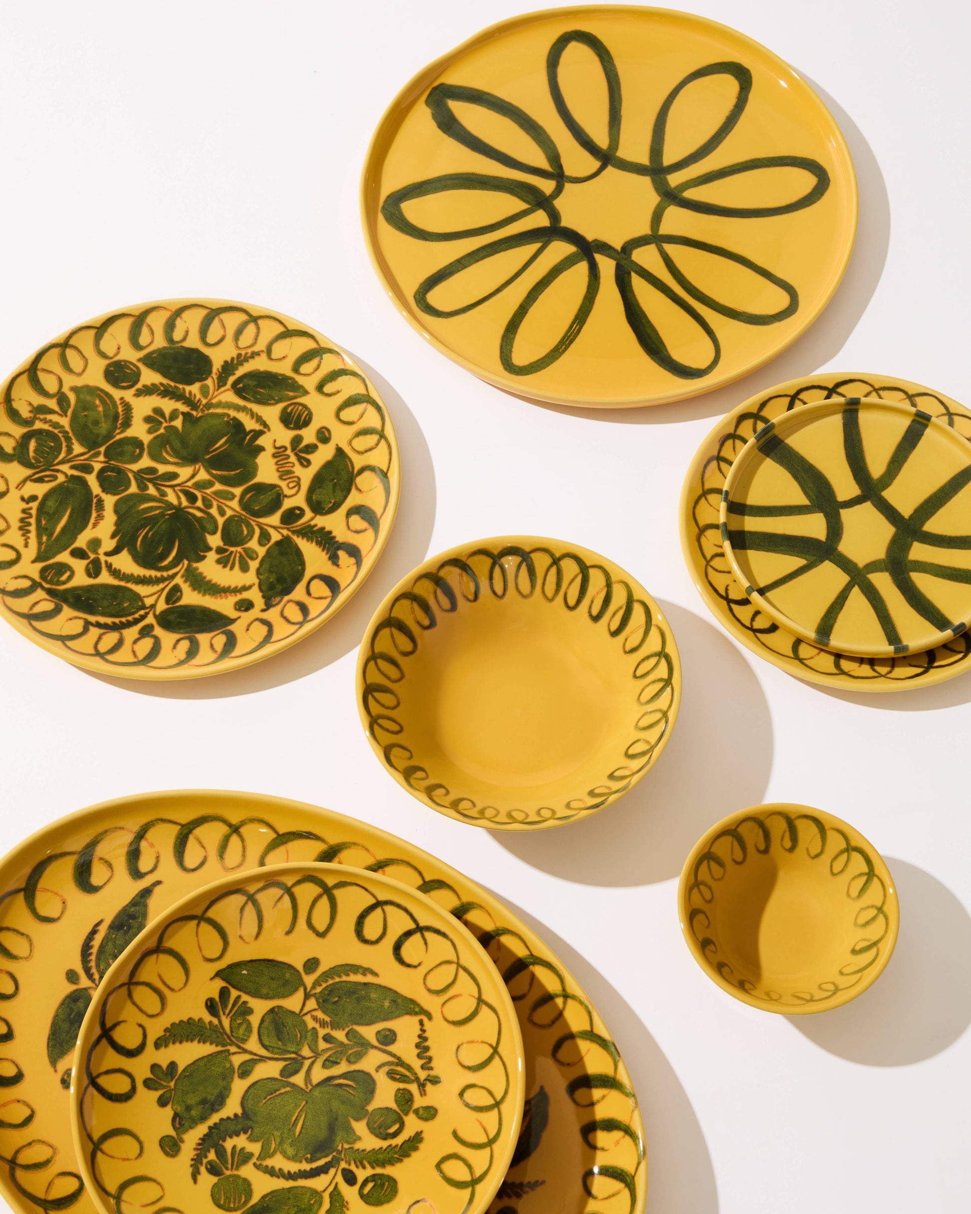 Set of yellow ceramic plates with green floral patterns on a white background