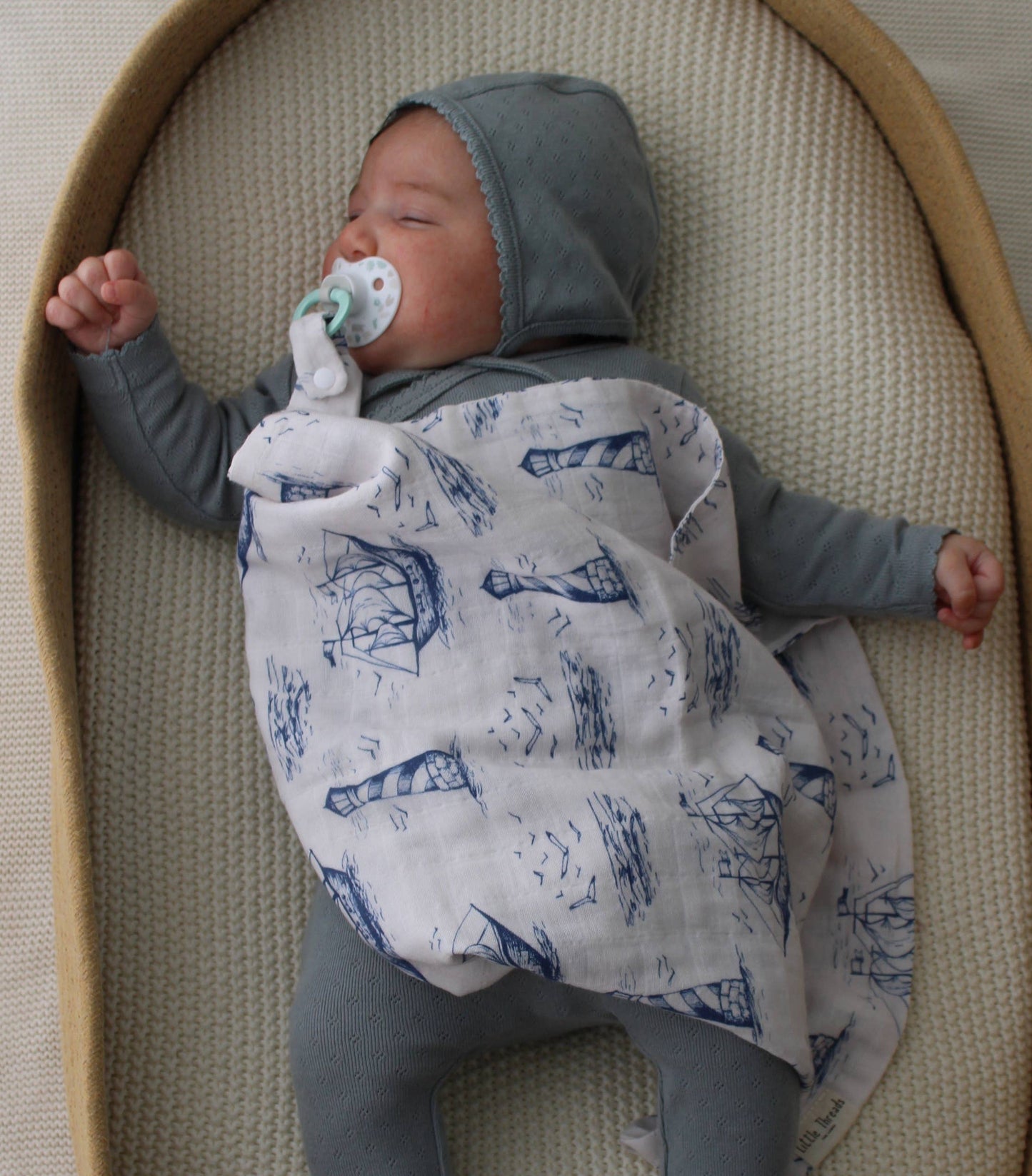 Baby sleeping in a bassinet with a gray blanket and blue pants