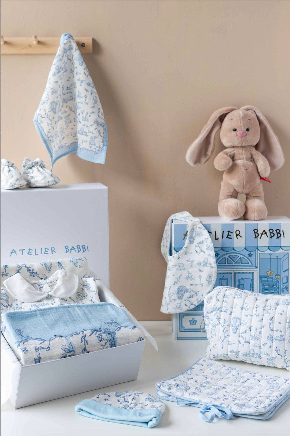 Baby crib set with blue and white patterns, including a blanket, pillow, and toy, on a beige background.