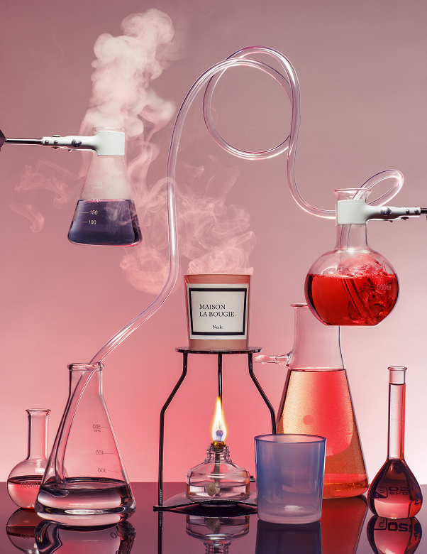 Laboratory setup with flasks, candles, and a flame on a reflective surface.