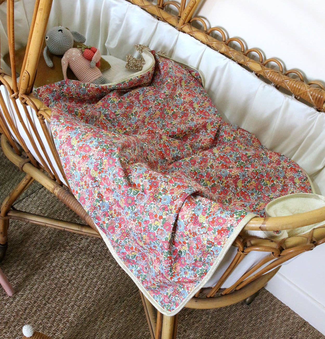 Floral-patterned blanket on a wicker crib with toys around