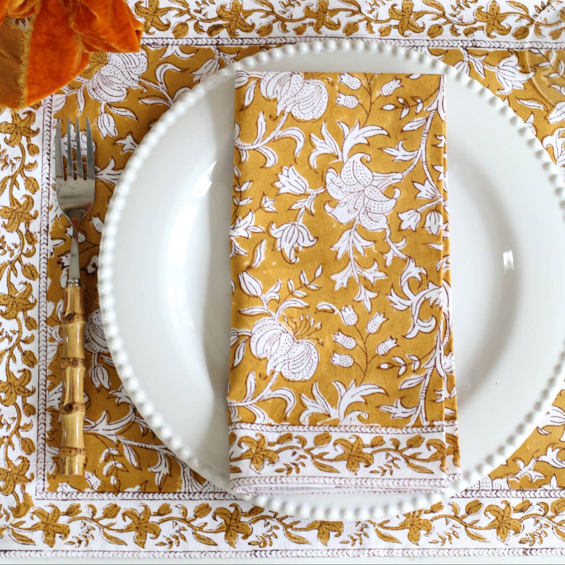 Decorative table setting with floral centerpiece, white plates, and gold-patterned placemats.